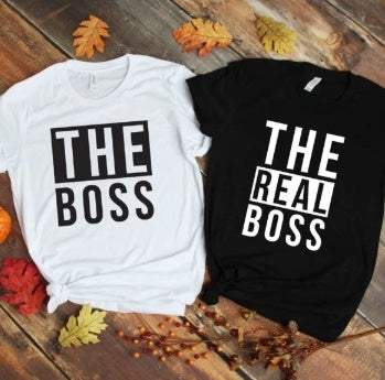 Pair of men's T-shirts with "THE BOSS" and "THE REAL BOSS" prints in black and white colors on wooden floor with autumn leaves