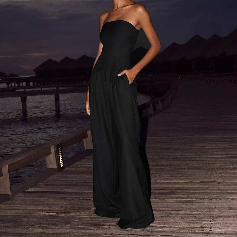 Woman wearing elegant black losse tube-top jumpsuit standing on wooden pier at dusk