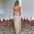 Vrouw draagt sexy een-schouder open rug jurk in beige, staand tussen rozenblaadjes en kaarsen.
