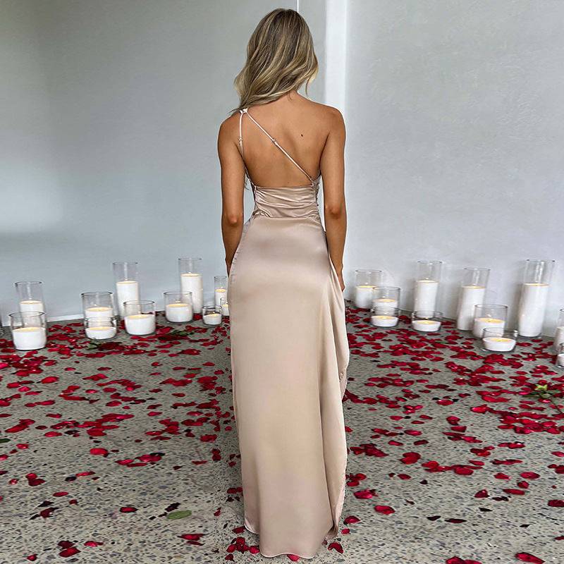 Vrouw draagt sexy een-schouder open rug jurk in beige, staand tussen rozenblaadjes en kaarsen.