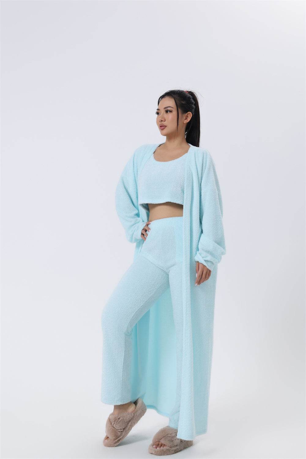 vrouwelijk model draagt lichtblauwe zachte en pluizige 3-delige set met crop top, broek en lange cardigan