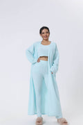 vrouw in lichtblauwe zachte gebreide 3-delige set met lange cardigan, crop top en wijde broekspijpen, comfortabele loungekleding
