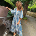 vrouw in zomerse dames vintage jurk met blauwwitte ruitpatroon buiten naast auto